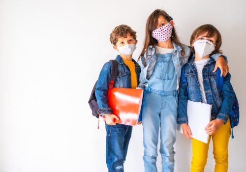 kids-with-facemasks-holding-their-school-belongings-standing-against-wall-covid-19