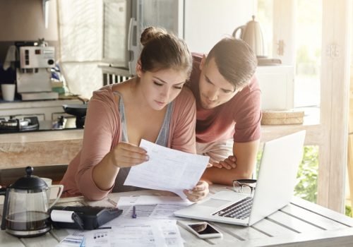young-couple-managing-finances-reviewing-their-bank-accounts-using-laptop-computer-and-calculator-at-modern-kitchen-woman-and-man-doing-paperwork-together